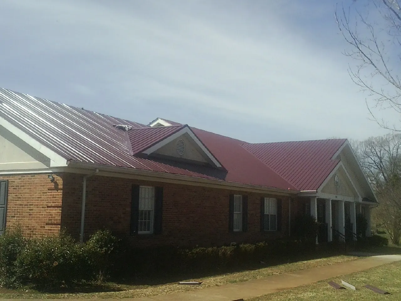 Red metal roof with gabled entries on a long brick building, from a Hail Damage Roof Repair job in Abingdon